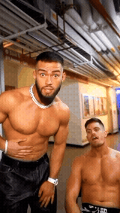 A Shirtless Man Is Standing Next To A Shirtless Man In A Hallway . GIF