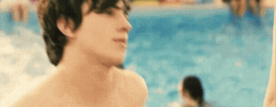 A Shirtless Man Is Standing Next To A Swimming Pool Looking At The Camera . GIF
