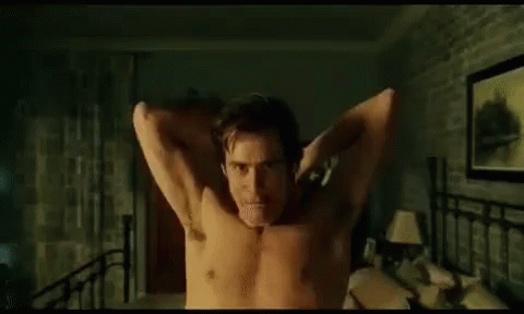 A Shirtless Man Is Standing On A Bed With His Arms Outstretched In A Bedroom . GIF