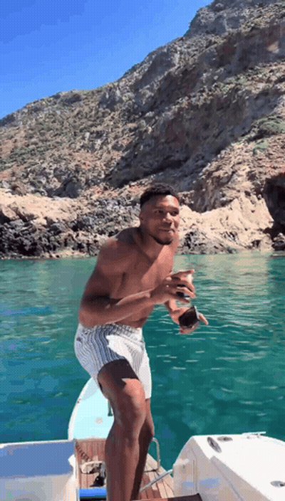 A Shirtless Man Is Standing On A Boat In The Ocean GIF