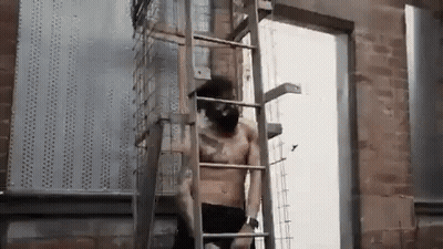 A Shirtless Man Is Standing On A Ladder . GIF
