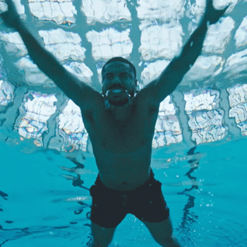 A Shirtless Man Is Swimming In A Pool With His Arms In The Air GIF