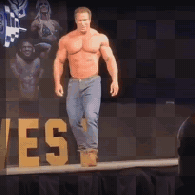 A Shirtless Man Is Walking Down A Stage With A Sign That Says Yes In The Background GIF