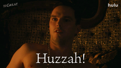 A Shirtless Man Laying On A Bed With The Words Huzzah On The Bottom Right GIF