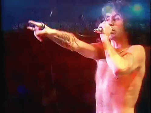 A Shirtless Man Singing Into A Microphone While Pointing GIF