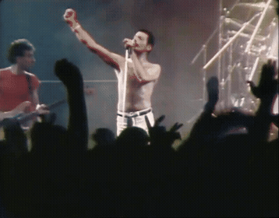 A Shirtless Man Singing Into A Microphone With His Fist In The Air GIF