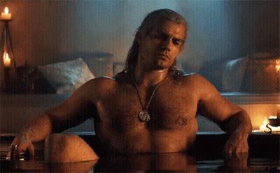 A Shirtless Man Sits In A Bathtub With Candles In The Background GIF