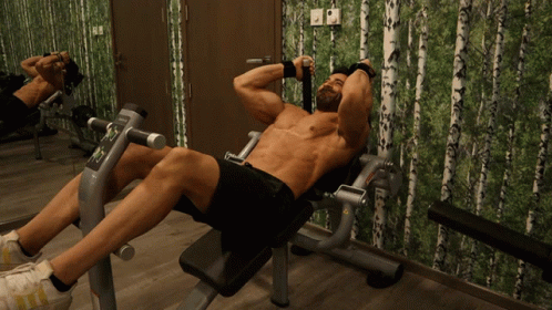 A Shirtless Man Sits On A Bench In Front Of A Mirror GIF