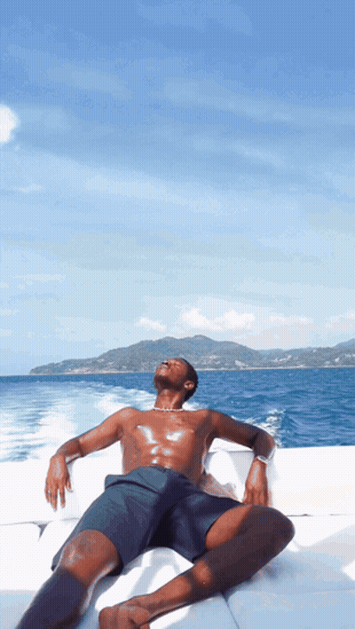 A Shirtless Man Sits On A Boat Looking Up At The Sky GIF
