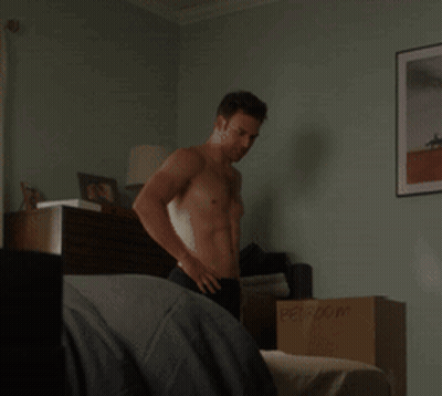 A Shirtless Man Stands In A Bedroom Next To A Cardboard Box Labeled Person GIF