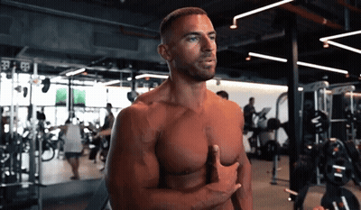 A Shirtless Man Stands In A Gym With His Hands On His Chest GIF