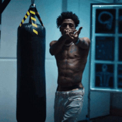 A Shirtless Man Stands In Front Of A Boxing Bag GIF
