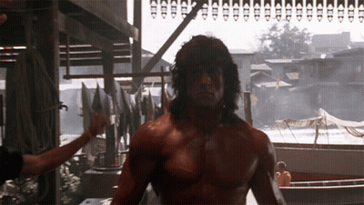 A Shirtless Man Stands In Front Of A Row Of Boats And Buildings GIF