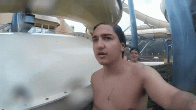 A Shirtless Man Stands In Front Of A Water Slide At A Water Park GIF