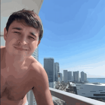 A Shirtless Man Stands On A Balcony Overlooking The City GIF