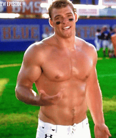 A Shirtless Man Stands On A Field In Front Of A Blue Banner GIF