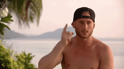 A Shirtless Man Wearing A Baseball Cap Is Pointing At Something GIF