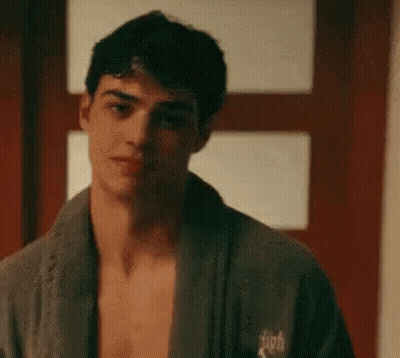 A Shirtless Man Wearing A Bathrobe Is Standing In Front Of A Door . GIF