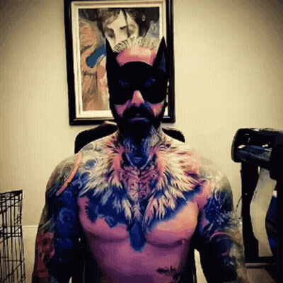 A Shirtless Man Wearing A Cat Mask And Feathers On His Chest GIF