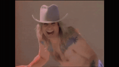 A Shirtless Man Wearing A Cowboy Hat Is Laughing . GIF