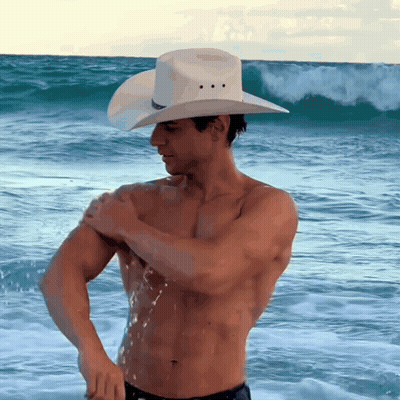 A Shirtless Man Wearing A Cowboy Hat Is Standing In The Ocean GIF