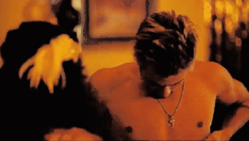 A Shirtless Man Wearing A Cross Necklace Looks Down At Something GIF