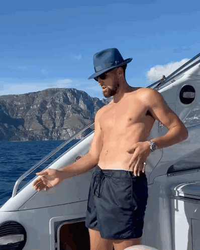 A Shirtless Man Wearing A Hat And Sunglasses Stands On A Boat GIF