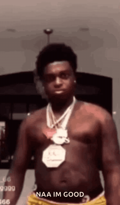 A Shirtless Man Wearing A Necklace And Shorts Is Standing In A Room With His Shirt Off . GIF