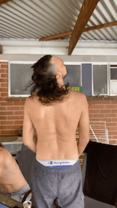 A Shirtless Man Wearing A Pair Of Champion Shorts Stands In Front Of A Brick Wall GIF