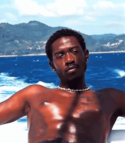 A Shirtless Man Wearing A Pearl Necklace Is Sitting On A Boat In The Ocean GIF