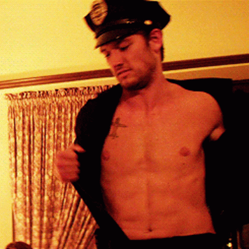 A Shirtless Man Wearing A Police Hat Takes Off His Jacket GIF