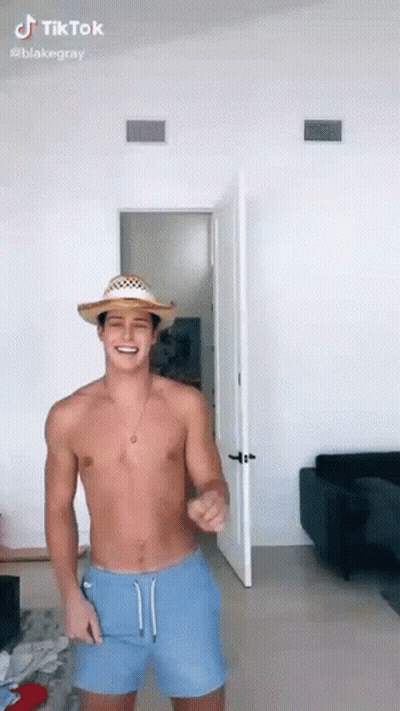 A Shirtless Man Wearing A Straw Hat And Blue Shorts Is Dancing In A Room . GIF