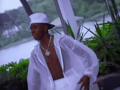 A Shirtless Man Wearing A White Hat And A Necklace With The Letter R On It Is Standing In Front Of A Body Of Water GIF