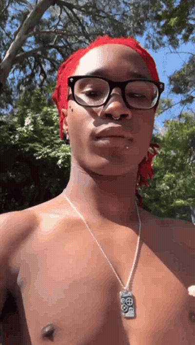 A Shirtless Man Wearing Glasses And A Necklace Is Standing In Front Of Trees . GIF