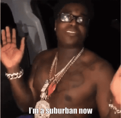 A Shirtless Man Wearing Glasses And A Necklace With The Words `` I 'M A Suburban Now '' On It . GIF
