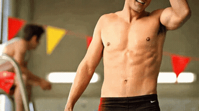 A Shirtless Man Wearing Nike Swim Trunks Stands In Front Of A Swimming Pool GIF