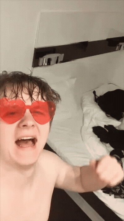 A Shirtless Man Wearing Red Heart Shaped Sunglasses Is Standing In Front Of A Bed GIF
