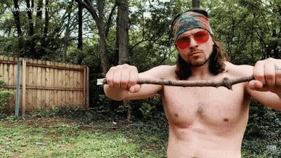 A Shirtless Man Wearing Sunglasses And A Bandana Is Holding A Stick In His Hands GIF