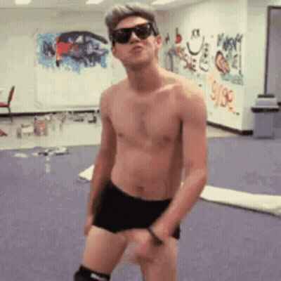 A Shirtless Man Wearing Sunglasses Is Dancing In A Room With Graffiti On The Wall GIF