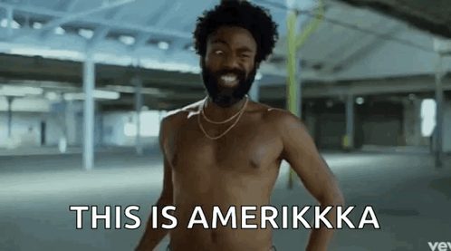 A Shirtless Man With A Beard And A Necklace Says This Is Amerikkka GIF