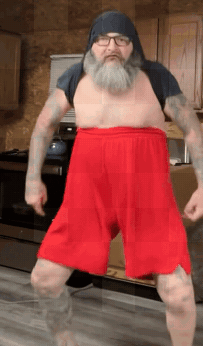 A Shirtless Man With A Beard And Red Shorts Is Dancing GIF