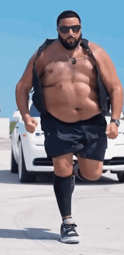 A Shirtless Man With A Beard And Sunglasses Is Running In Front Of A White Car GIF