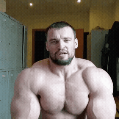 A Shirtless Man With A Beard Is Flexing His Muscles In A Gym . GIF