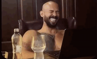 A Shirtless Man With A Beard Is Laughing While Sitting In Front Of A Laptop . GIF