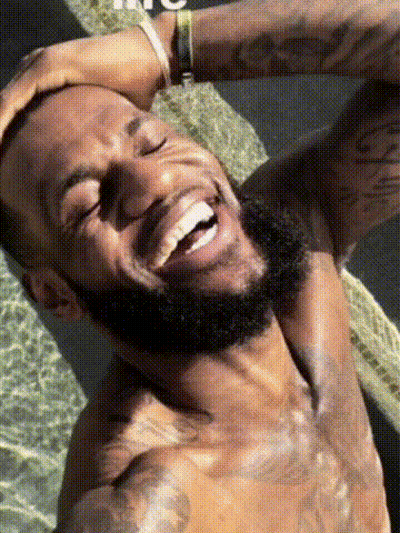 A Shirtless Man With A Beard Is Laughing With His Eyes Closed And His Hand On His Head . GIF