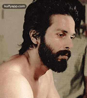 A Shirtless Man With A Beard Is Looking At A Woman . GIF