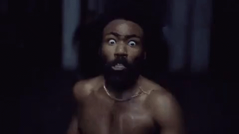 A Shirtless Man With A Beard Is Running In A Dark Room With His Eyes Wide Open . GIF