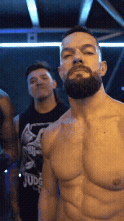 A Shirtless Man With A Beard Is Standing In A Dark Room With Other Men . GIF