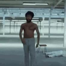 A Shirtless Man With A Beard Is Standing In A Room Holding A Stool . GIF
