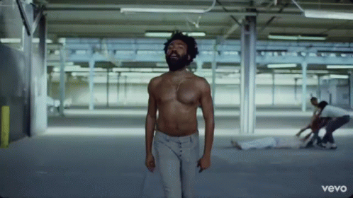 A Shirtless Man With A Beard Is Standing In A Warehouse . GIF